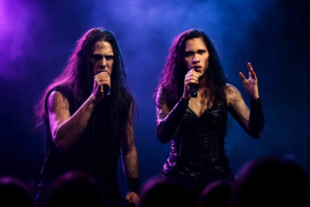 Dua vokalis band metal, cowok dan cewek, tampil di atas panggung dengan lampu dramatis